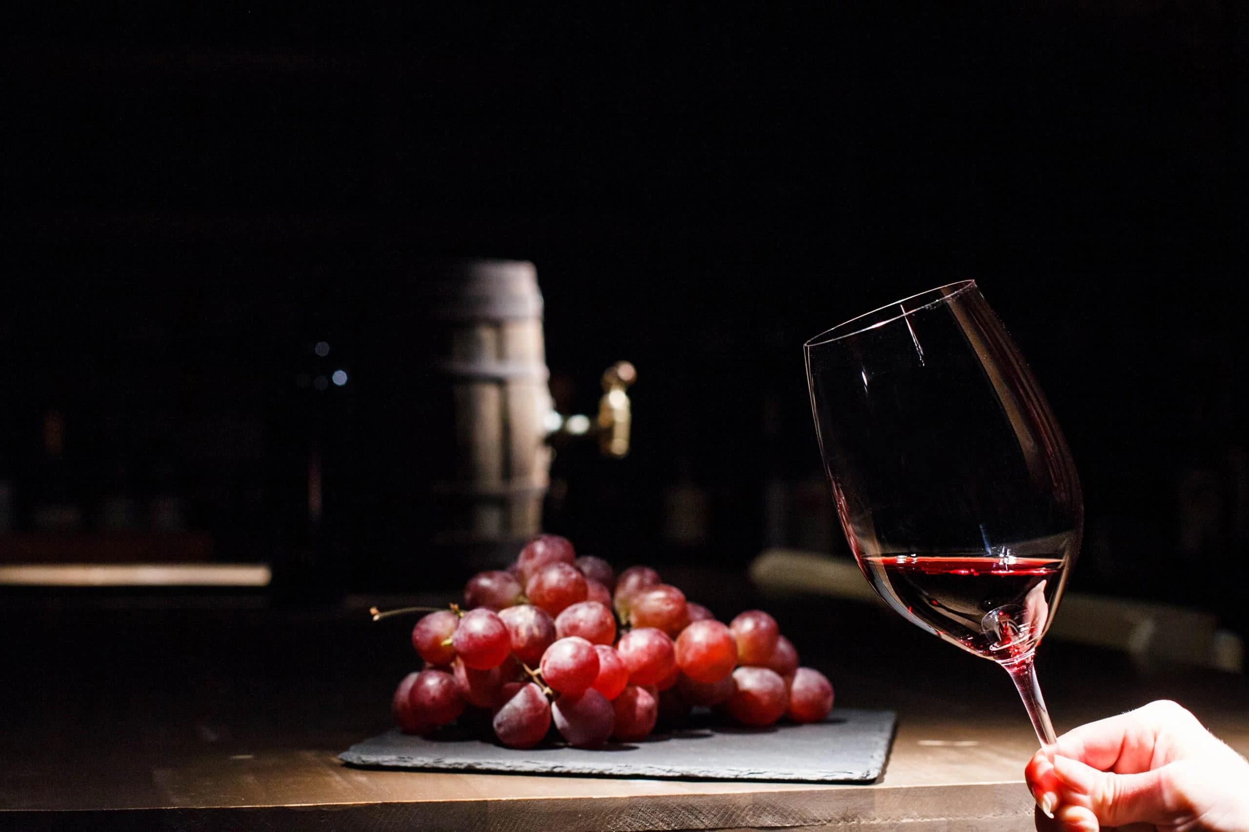 /wine-box-packaging/woman-holds-glass-wine-before-bunch-grape-lying-black-plate.webp